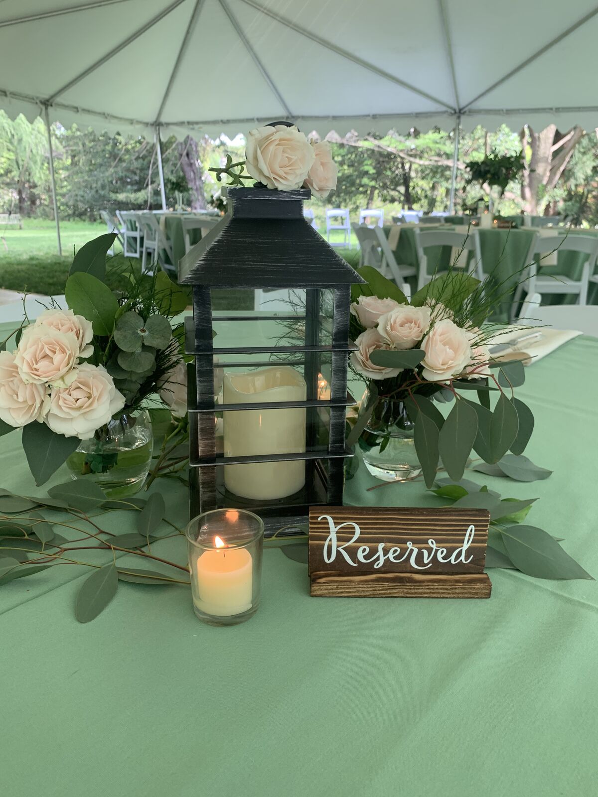 Outdoor tented reception table with a lantern-and-rose centerpiece and a Reserved sign