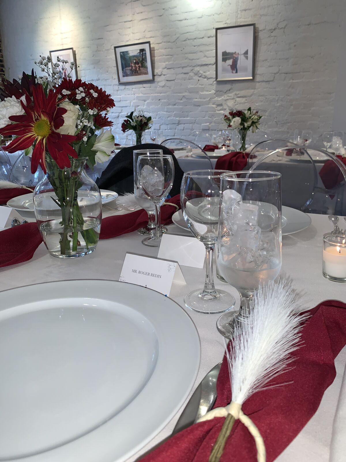 Intimate dinner tablescape with burgundy napkins and red floral accents against white brick