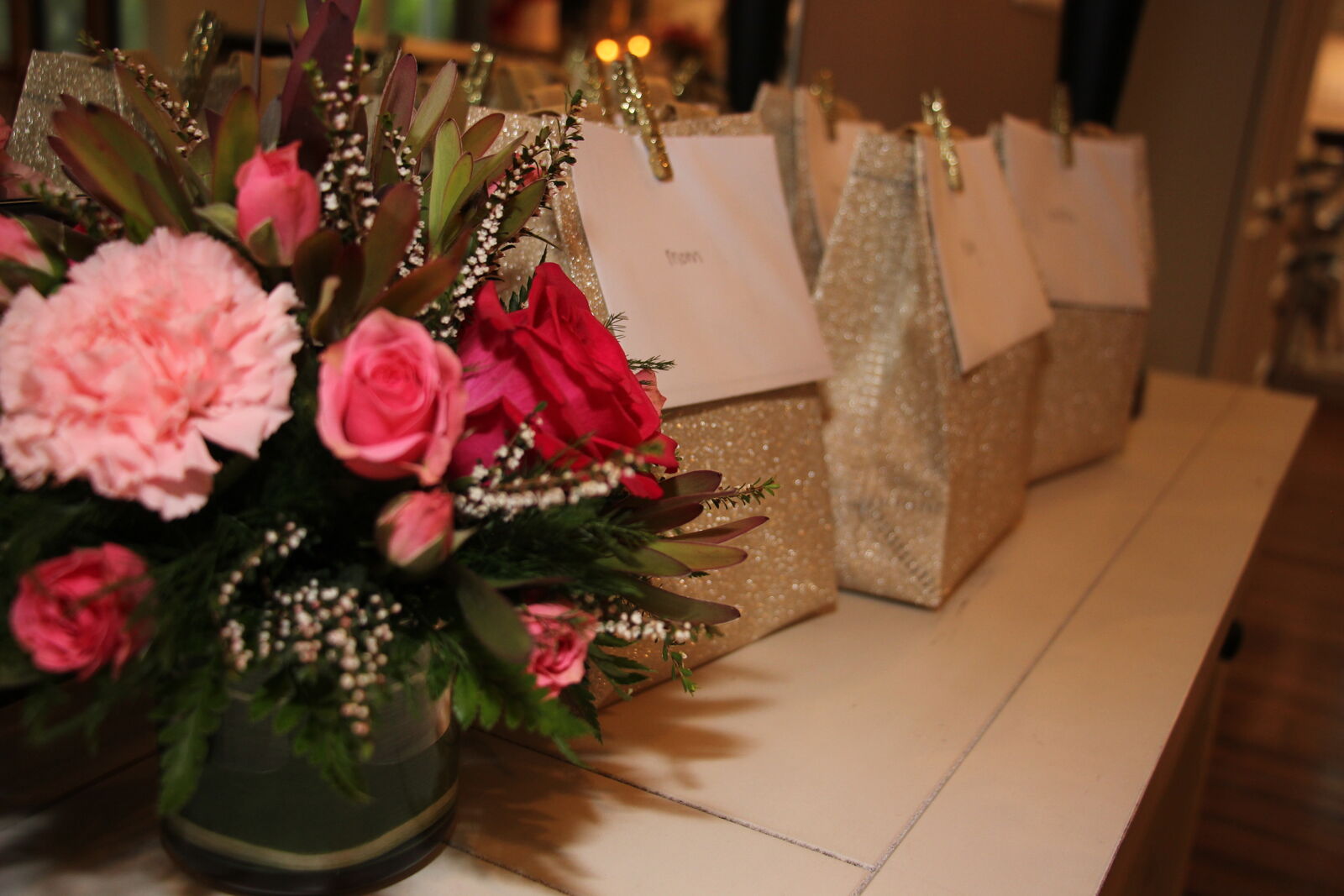 Pink and red floral arrangement beside a row of gold glitter guest favor bags