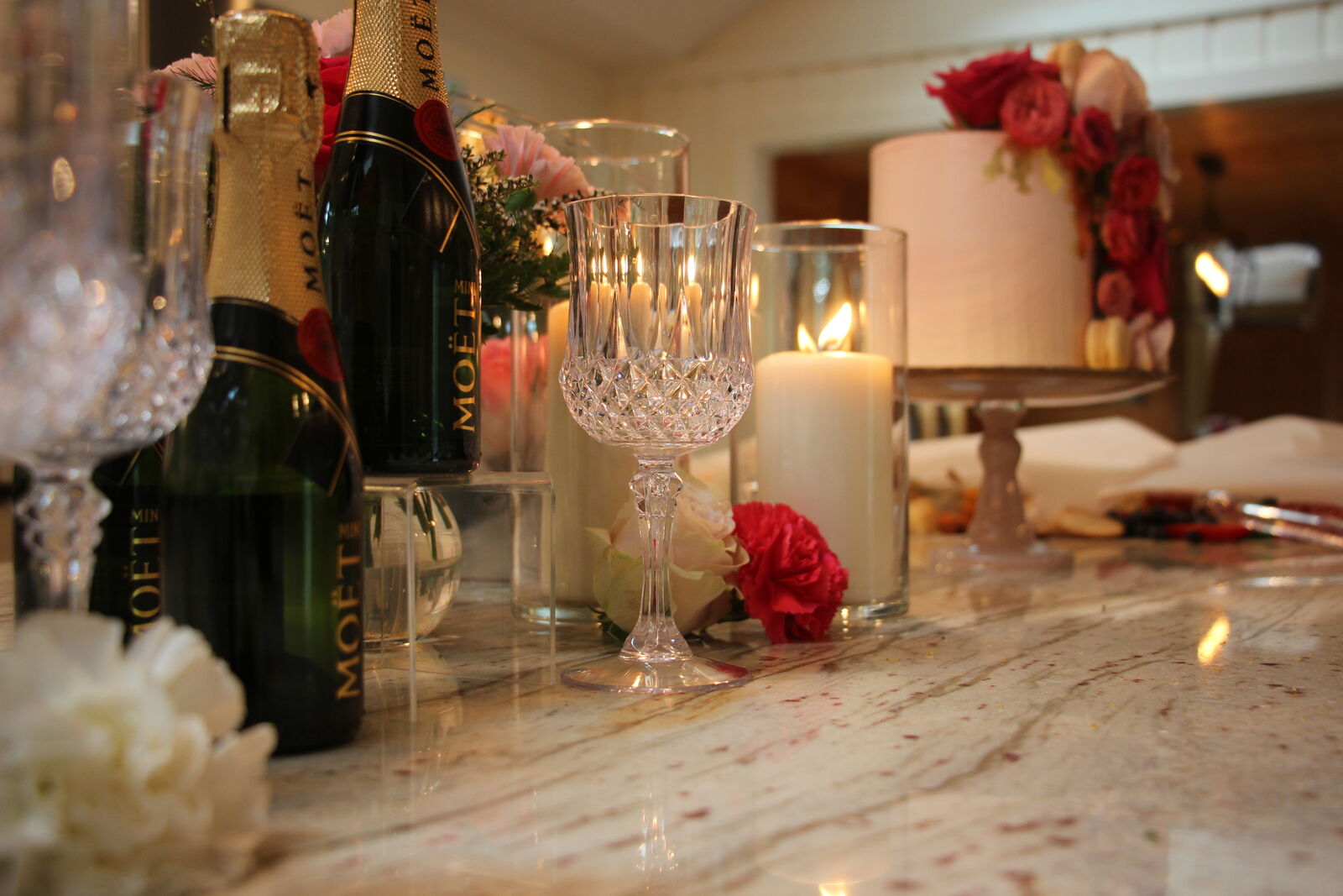 Mini champagne bottles, crystal goblets and candles beside a floral cake